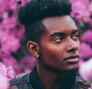 Headshot of a man staring off to the side against a backdrop of pink flowers.