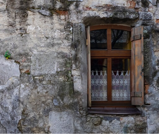 Wooden shutters of a window face out of a stone building.